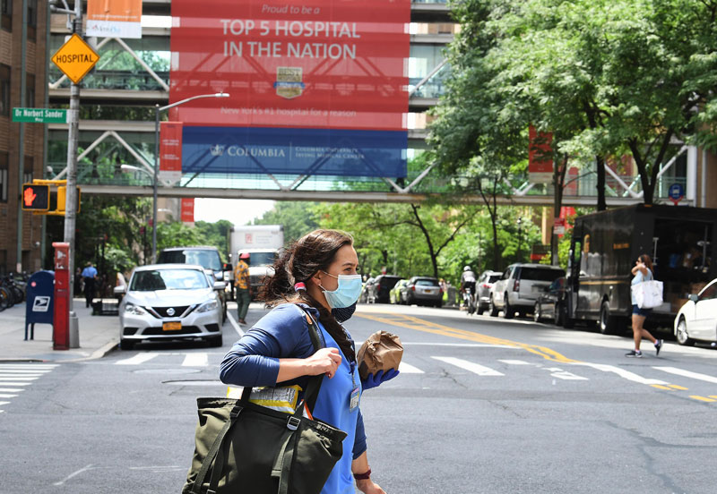 A woman in scrubs and PPE walking across the stree